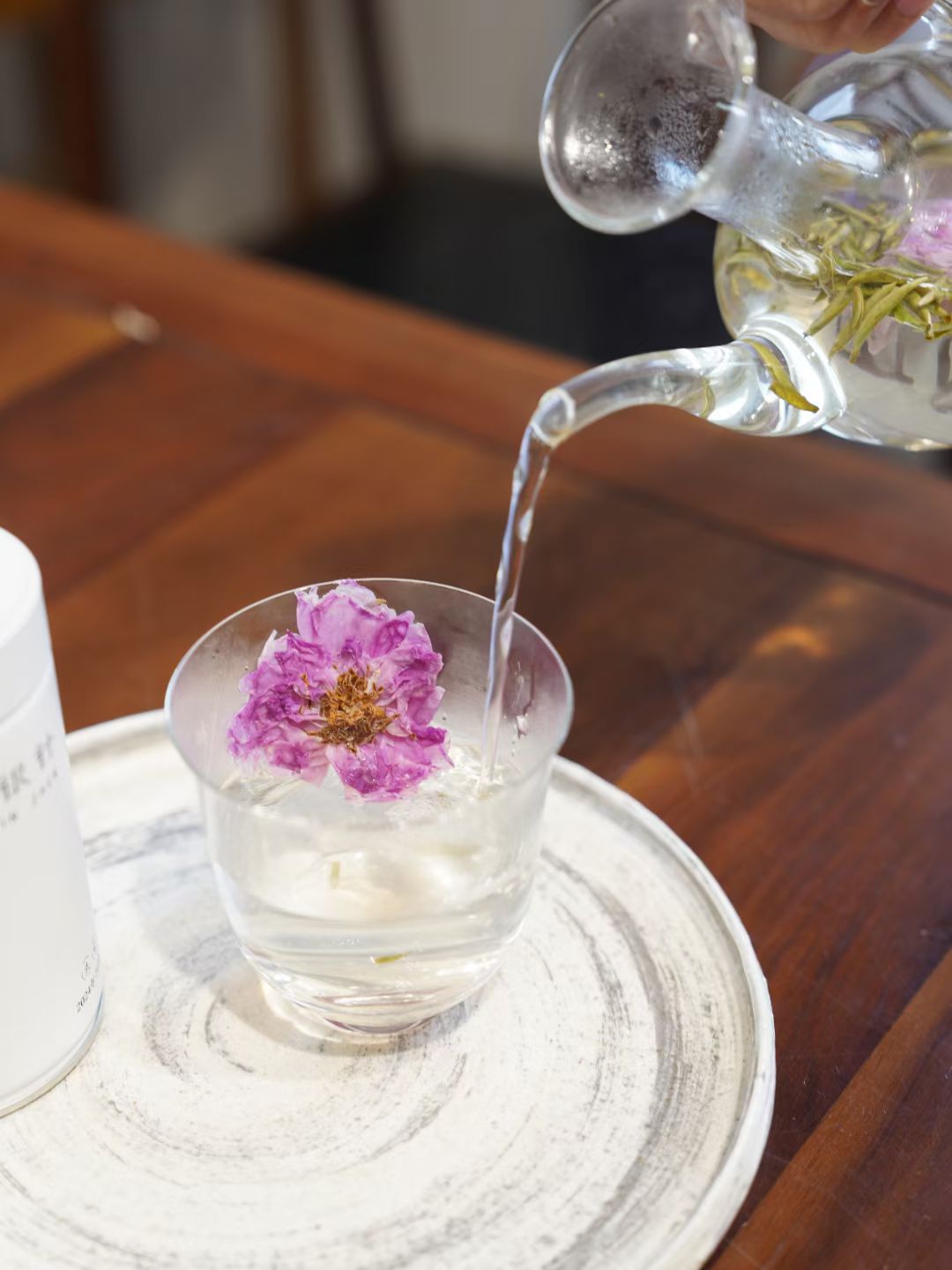 Tea being poured into a glass with a pink flower on a wooden table