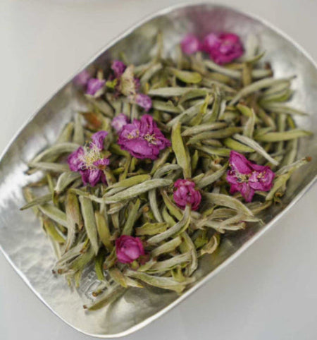 Green tea leaves with pink flowers on a metallic tray