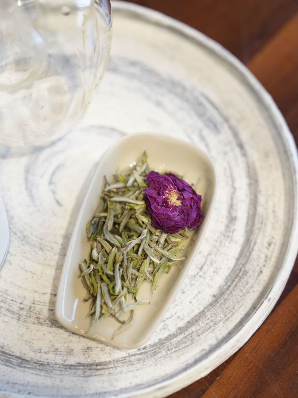 Tea leaves and a purple flower on a white ceramic dish with a blurred background