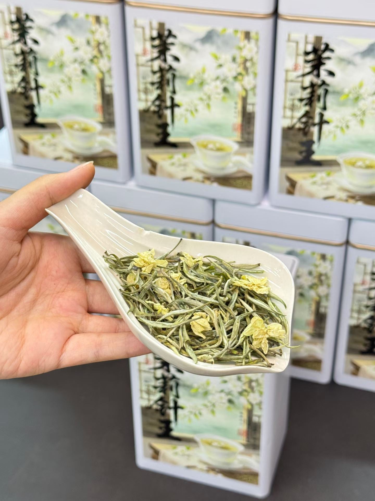 Hand holding a white scoop with green tea leaves in front of tea packaging