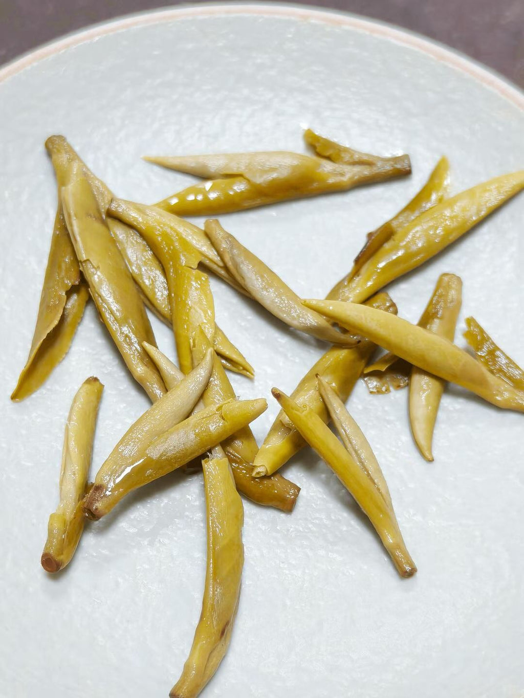 Dried yellow tea leaves on a white plate. Exhale — 2026 fresh harvest jasmine needle tea for anxiety and stress relief. Premium spring buds, intensely fragrant, cooling golden liquor. Breathe out.