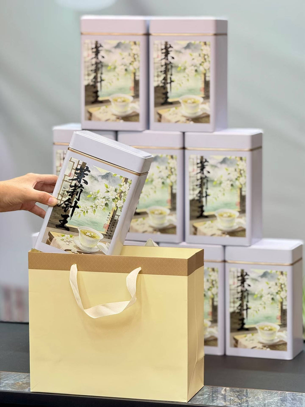 Gift box with a lid being held open, showing tea packaging inside, with more gift boxes stacked in the background.