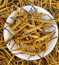 Golden Needle Black Tea 2026 New Harvest Dried yellow tea leaves on a white plate with more tea leaves in the background.