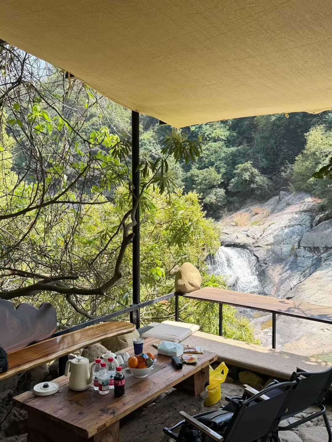 Outdoor setting with a wooden table, chairs, and a view of a waterfall.