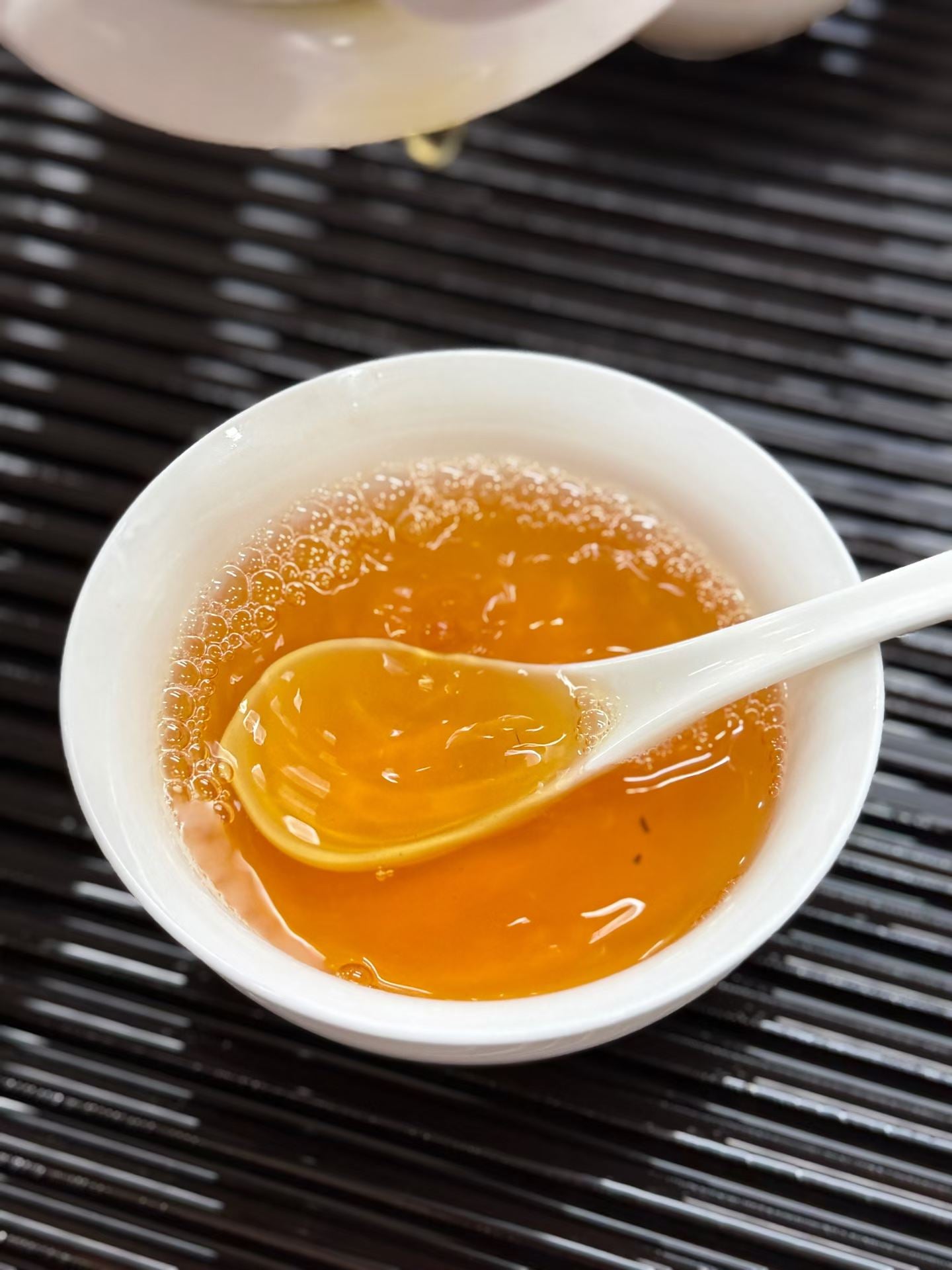 White bowl with a spoonful of honey on a black textured surface