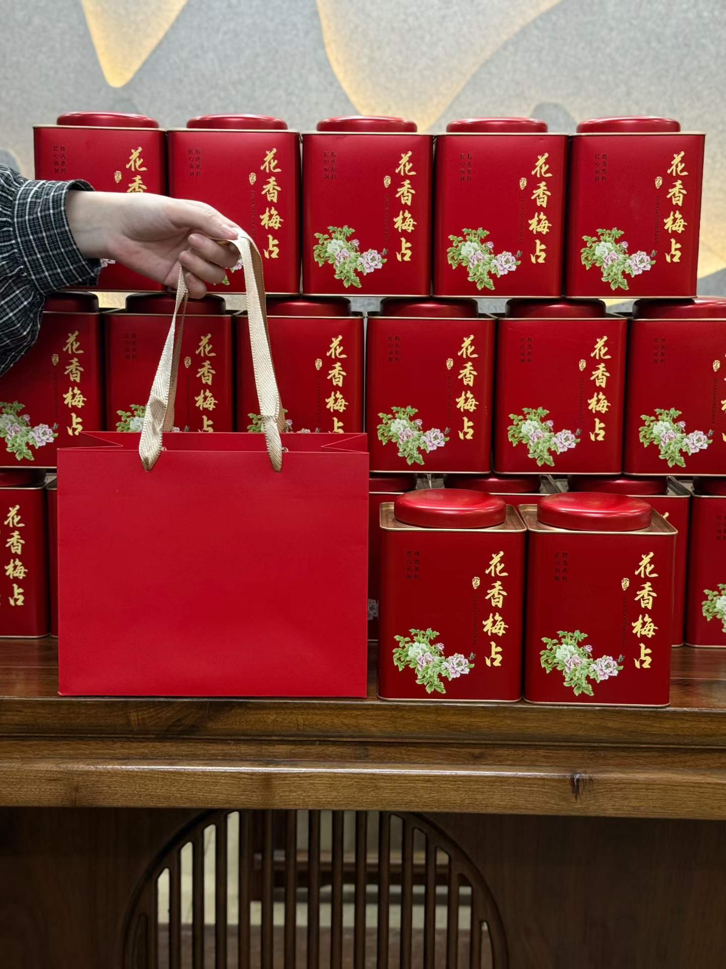 Red gift bag with floral design held by a hand in front of stacked red tea tins.