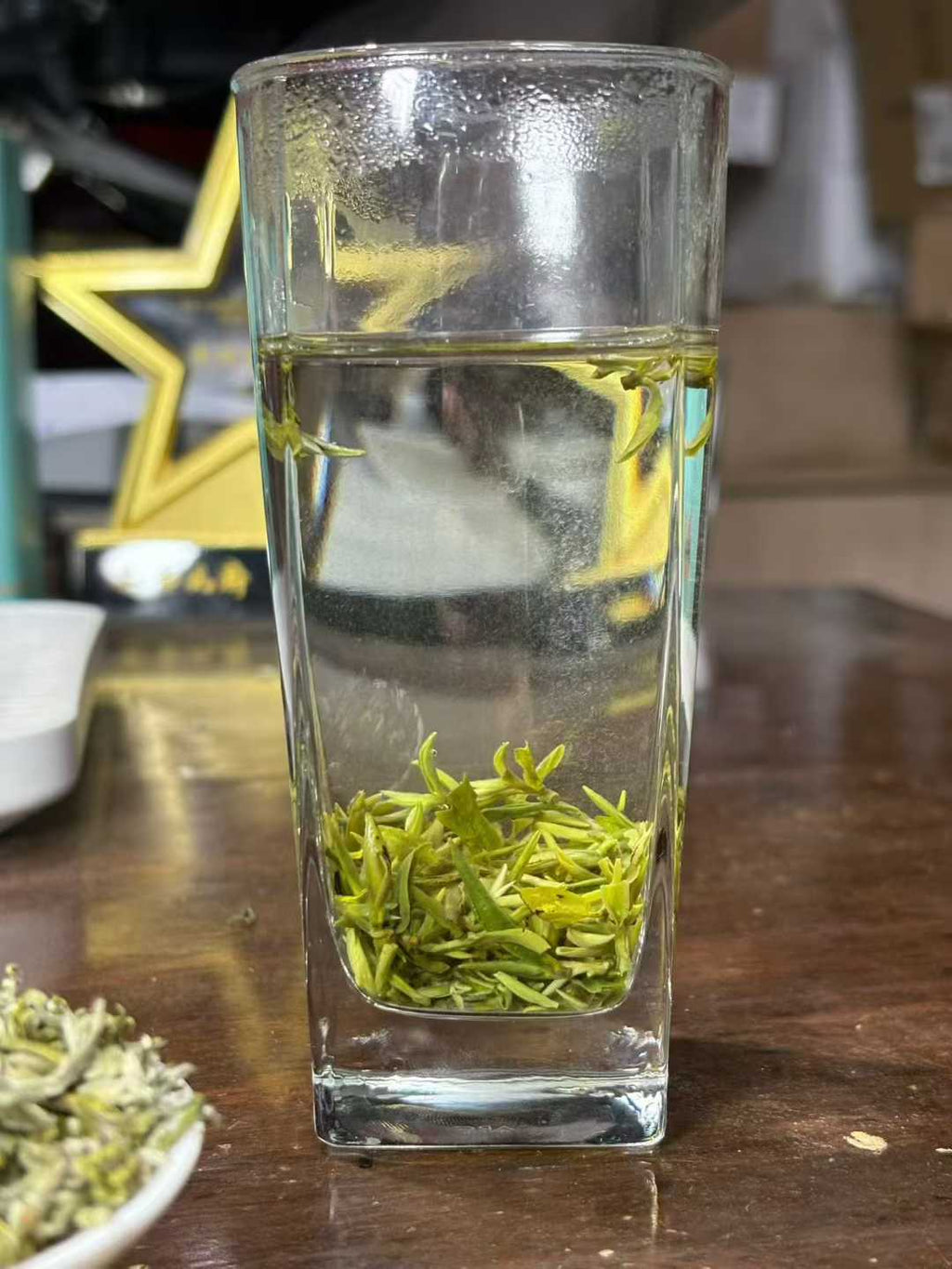 Green tea leaves in a clear glass of water on a wooden surface. Mengding Ganlu · 2026 First Harvest | Ancient Mountain Green Tea from Sichuan