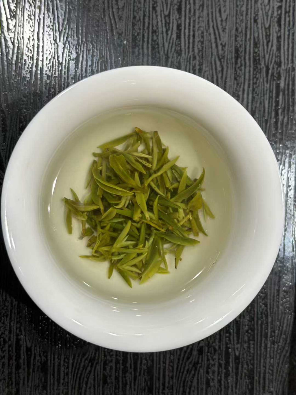 Mengding Ganlu · 2026 First Harvest | Ancient Mountain Green Tea from Sichuan. White bowl with green tea leaves on a dark textured surface