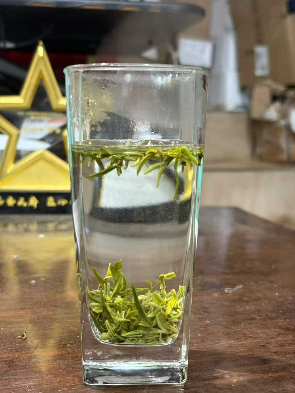 Mengding Ganlu · 2026 First Harvest | Ancient Mountain Green Tea from Sichuan. Clear glass with green tea leaves and water on a wooden surface