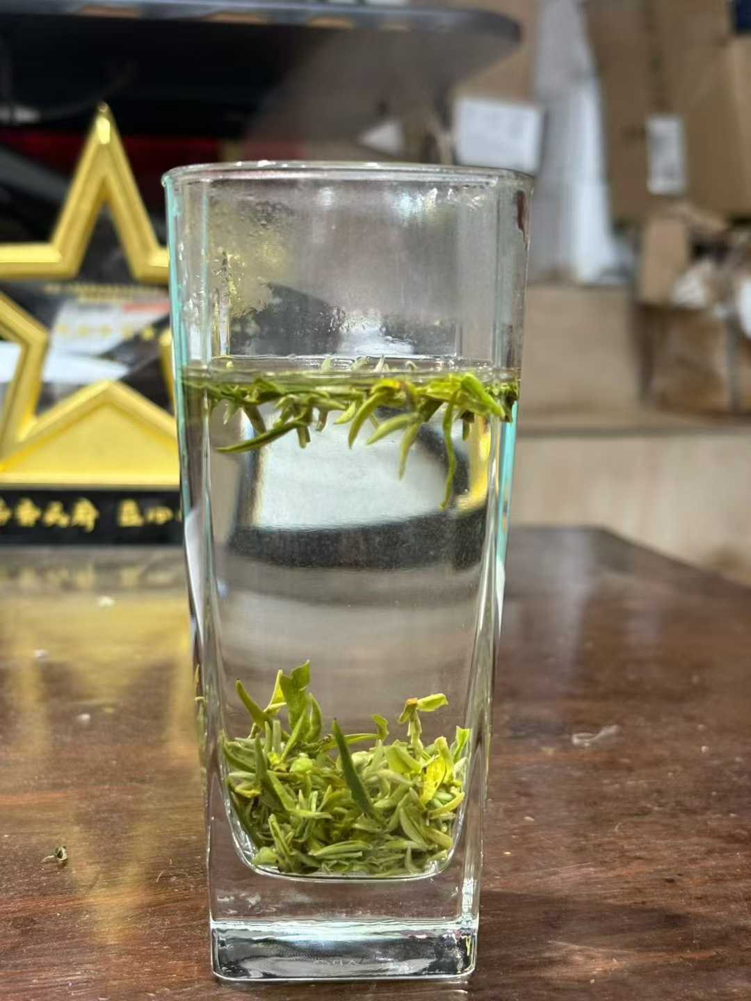 Mengding Ganlu · 2026 First Harvest | Ancient Mountain Green Tea from Sichuan. Clear glass with green tea leaves and water on a wooden surface