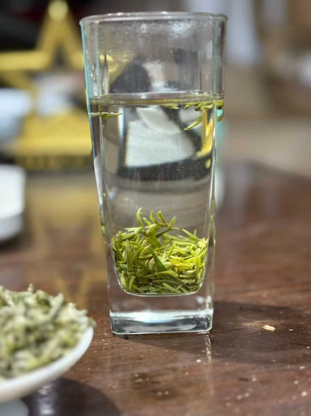 Mengding Ganlu · 2026 First Harvest | Ancient Mountain Green Tea from Sichuan. Clear glass with green tea leaves on a wooden surface