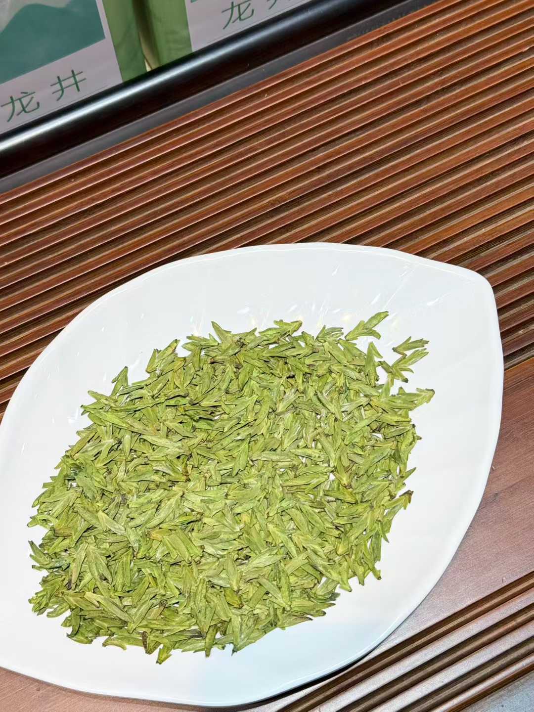 Longjing · 2026 Yu Qian Harvest | Pre-Rain Dragon Well Green Tea Green tea leaves on a white plate with a wooden surface in the background