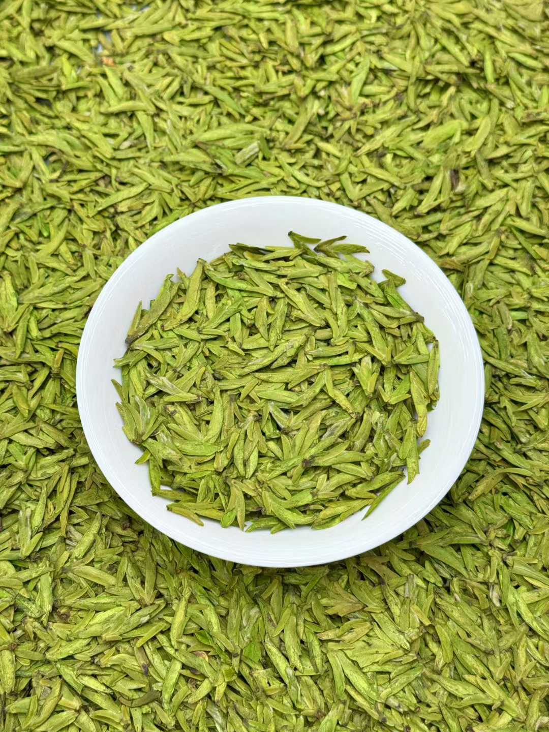 Longjing · 2026 Yu Qian Harvest | Pre-Rain Dragon Well Green Tea White bowl filled with green tea leaves on a bed of green tea leaves.