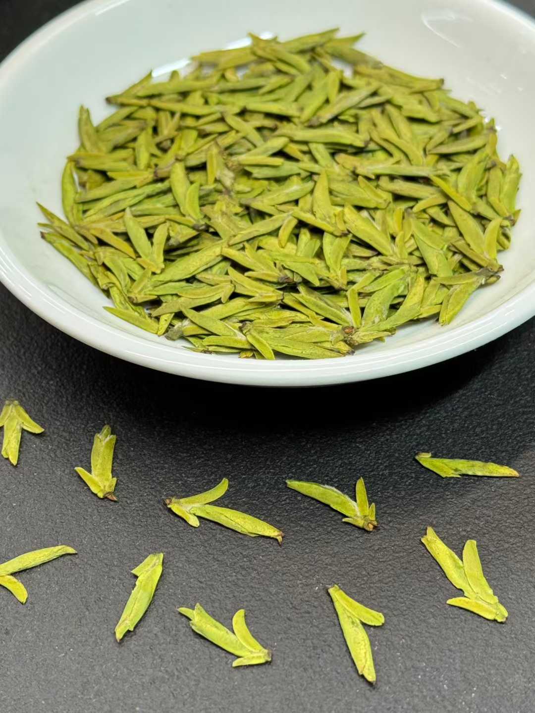 Green tea leaves in a white bowl on a dark surface