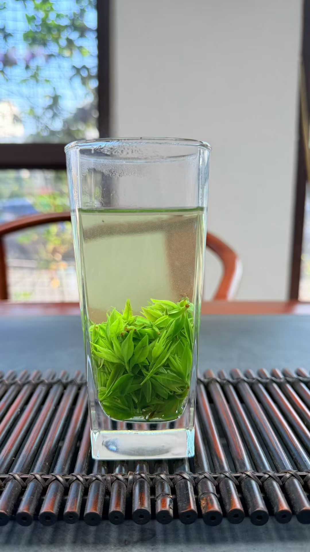 Small-Leaf Kuding · 2026 First Spring | Pure Rice-Bud Harvest, Clear glass with green tea leaves on a textured surface