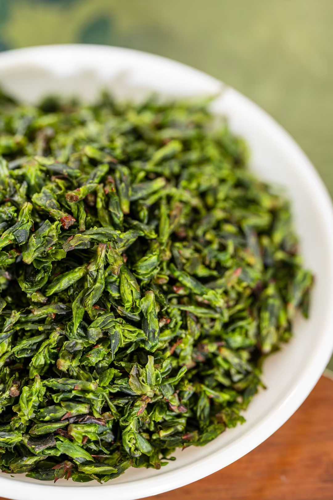 Small-Leaf Kuding · 2026 First Spring | Pure Rice-Bud Harvest, Close-up of green tea leaves in a white bowl with a blurred background