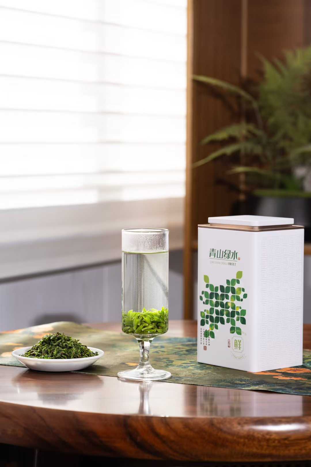 Small-Leaf Kuding · 2026 First Spring | Pure Rice-Bud Harvest, Glass of green tea with a box and bowl of tea leaves on a wooden table.