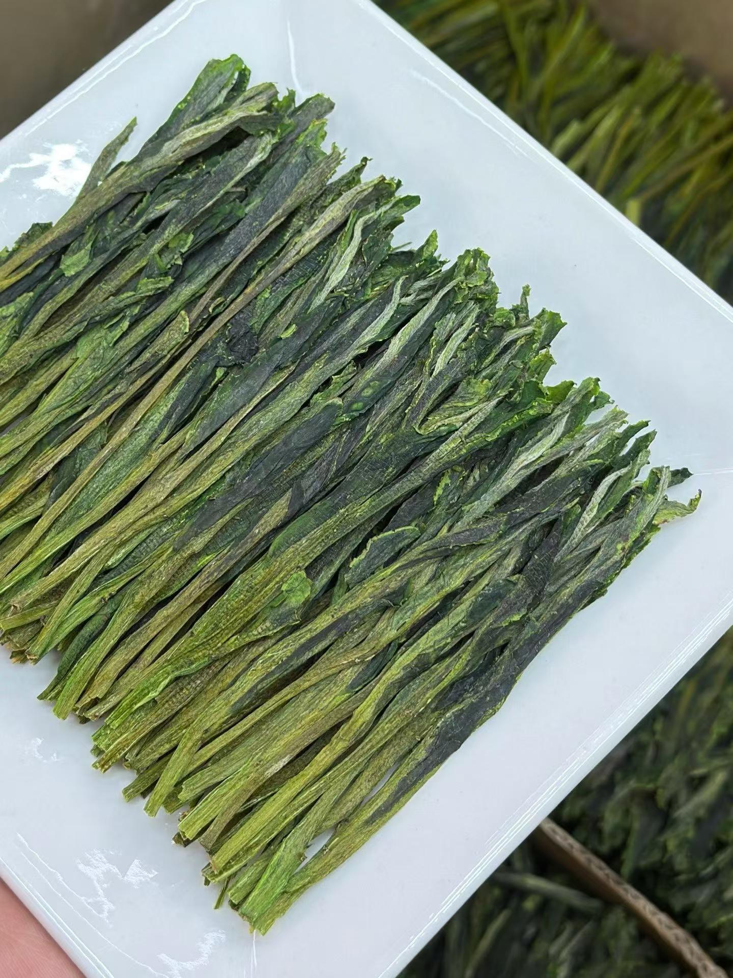 Dried green tea leaves on a white plat. Taiping Houkui hand-pressed green tea from Huangshan's high mountains. First-flush leaves, intangible-heritage craft, sword-straight blades, clear emerald liquor. Orchid-soft and sweet.