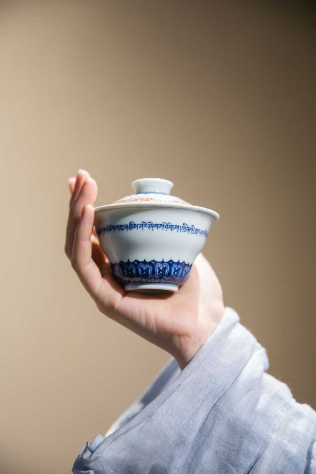 Hand holding a ceramic teacup with blue patterns against a plain background