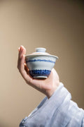 Hand holding a ceramic teacup with blue patterns against a plain background