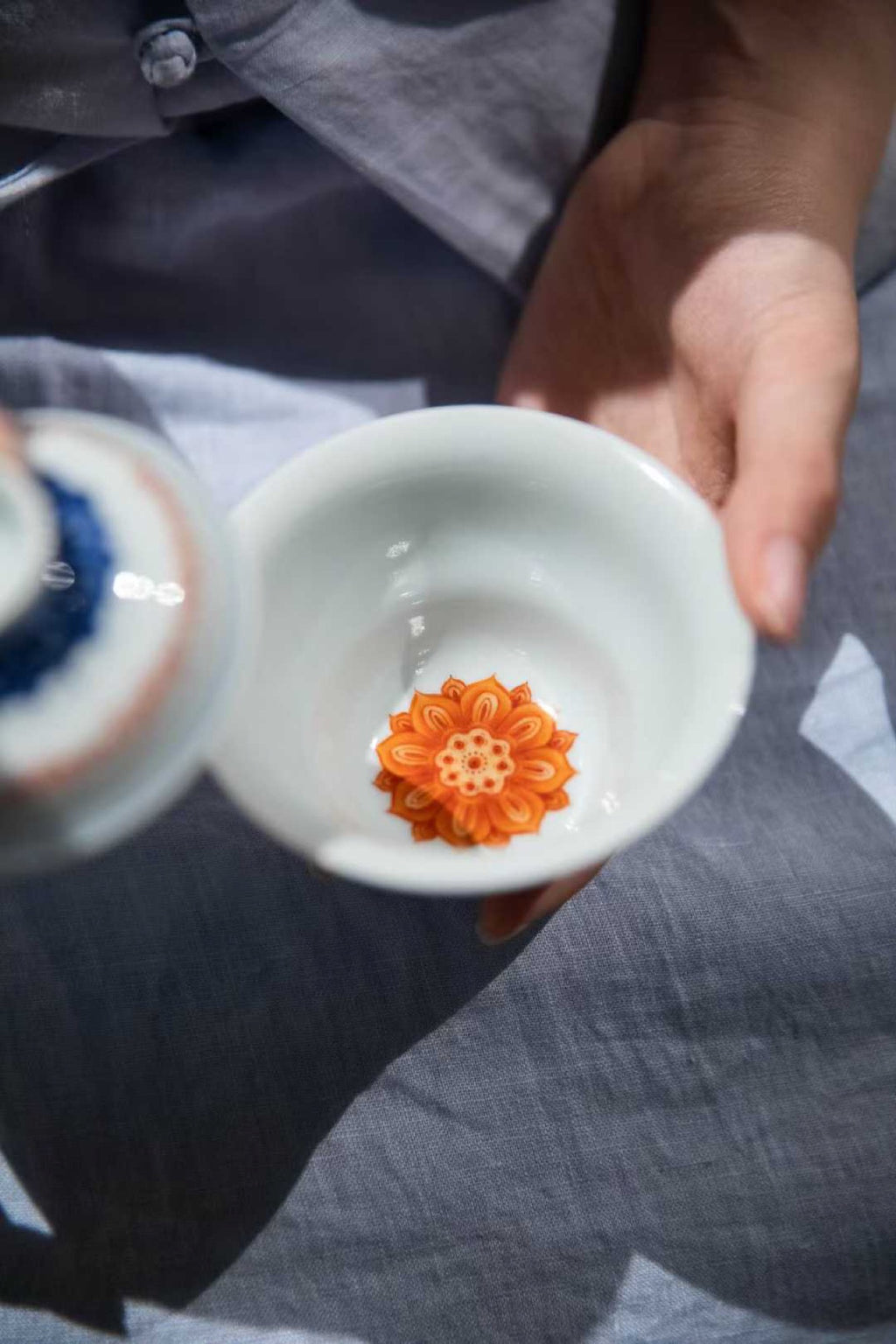 Person holding a white ceramic cup with an orange floral design on a gray fabric background