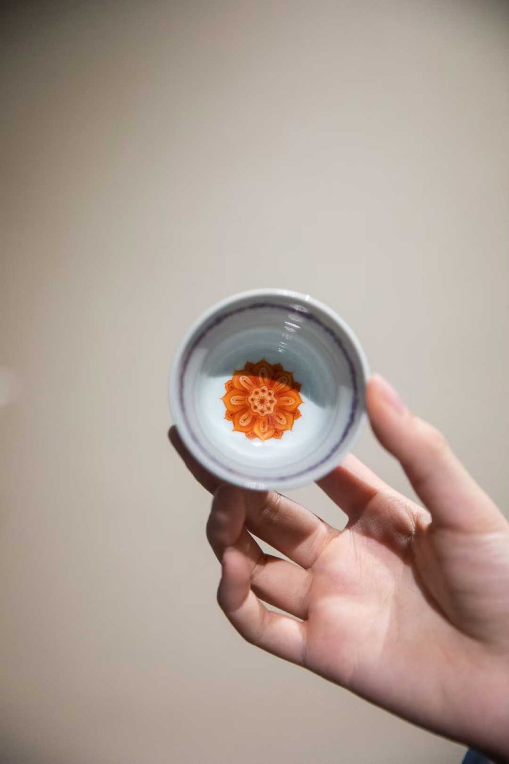 Hand holding a small container with a decorative orange flower design on a plain background