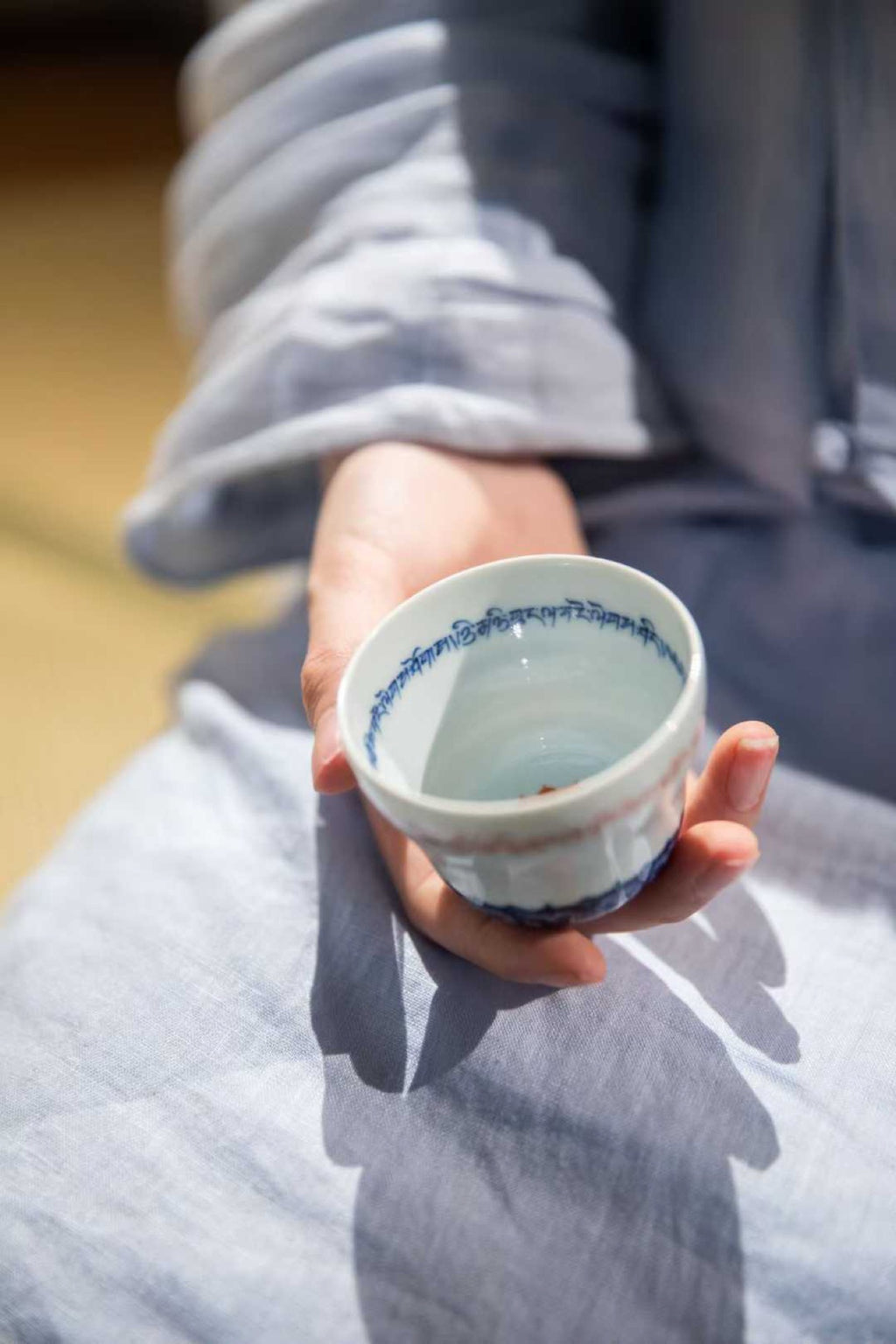 Person holding a small white ceramic cup with blue decorative elements.