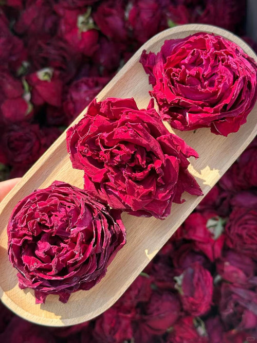 Three dried red roses on a wooden plate with more roses in the background. The deepest red Yunnan grows. In your cup.