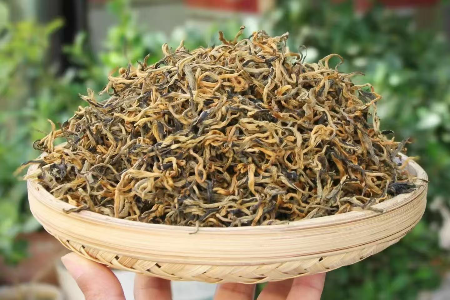 Dried tea leaves in a woven basket held by a hand with a blurred green background, 2026 Spring Glutinous Aroma Golden Bud Black Tea – High Bud Content (70–80%)