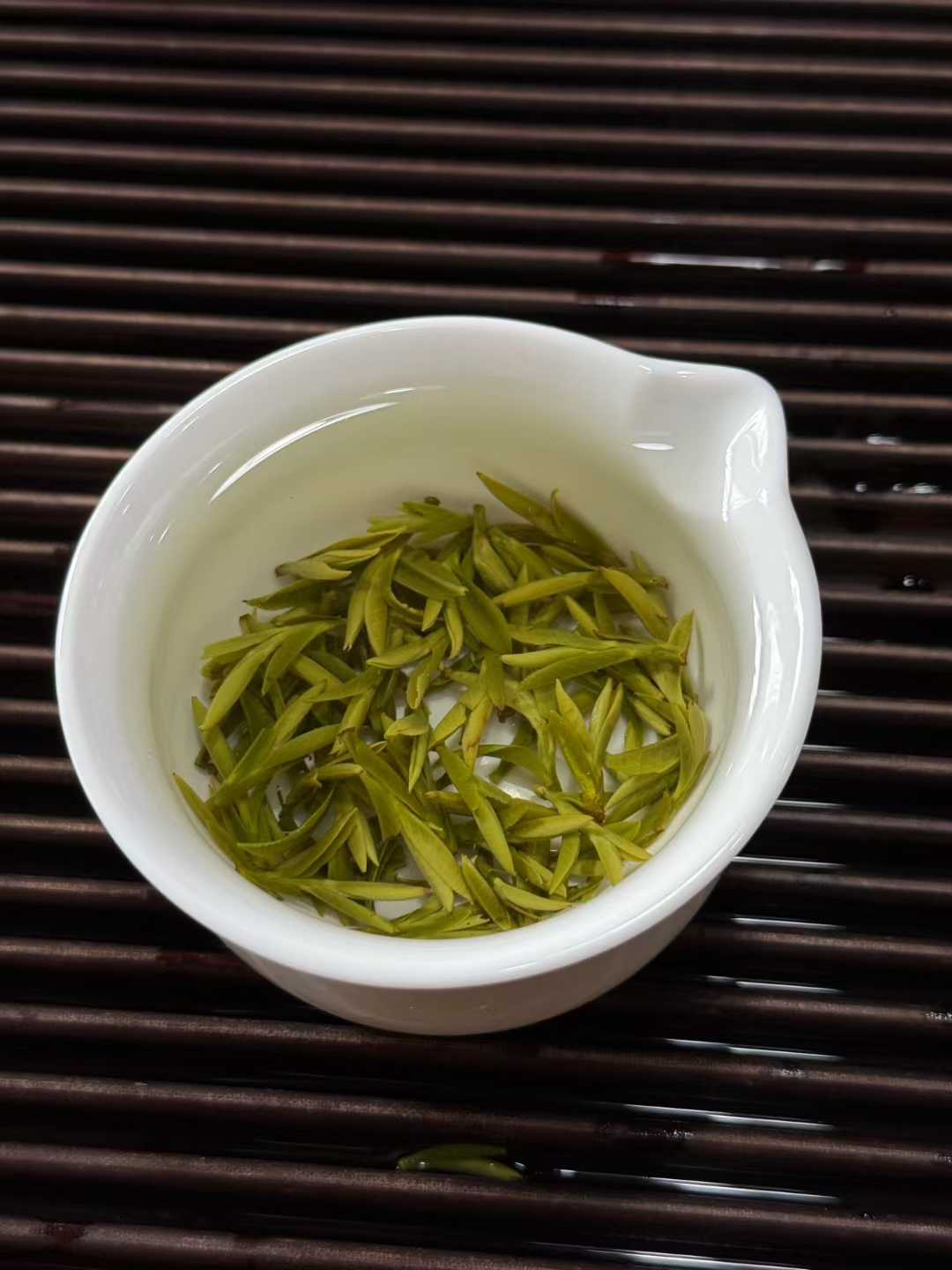 White bowl filled with green tea leaves on a dark wooden surface. 2026 First Harvest Huangshan Maofeng – Early Spring Imperial Green Tea