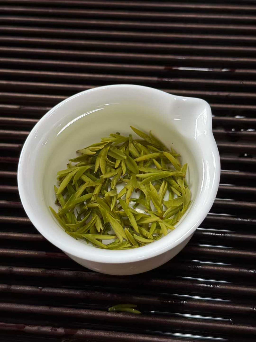 White ceramic cup filled with green tea leaves on a dark wooden surface.2026 First Harvest Huangshan Maofeng – Early Spring Imperial Green Tea