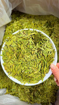 Green leafy substance in a white bowl held by a hand, with more of the substance around.