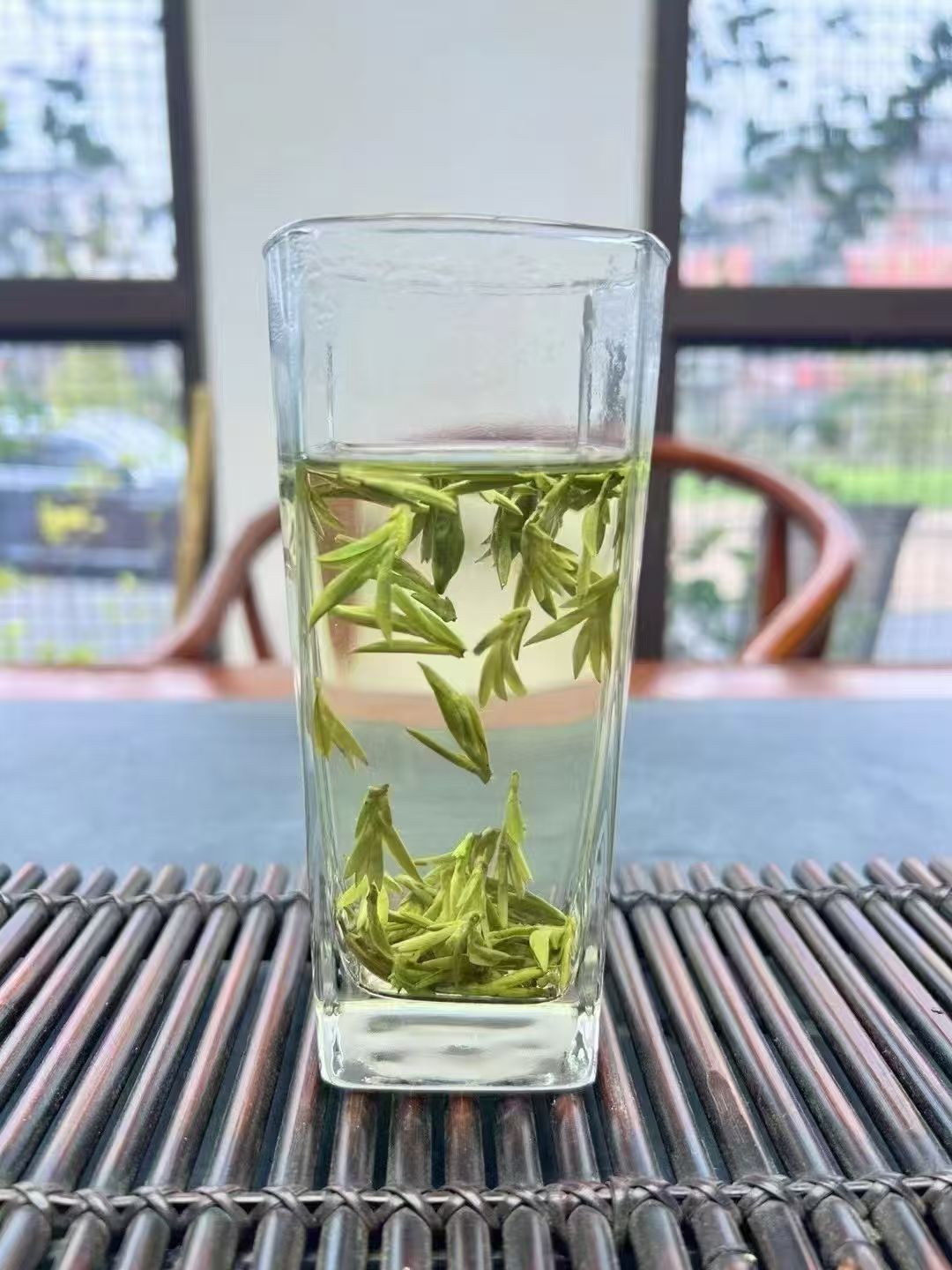 Clear glass with green tea leaves on a textured surface Selected from tender pre-Qingming buds, delivering a fresh vegetal sweetness layered with a signature chestnut aroma.