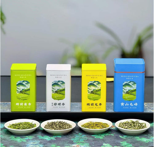 Four tea tins with scenic packaging on a table with bowls of tea leaves.Four of China’s most iconic spring green teas — harvested during the precious pre-Qingming season, when tea buds are at their most tender, fragrant, and vibrant.