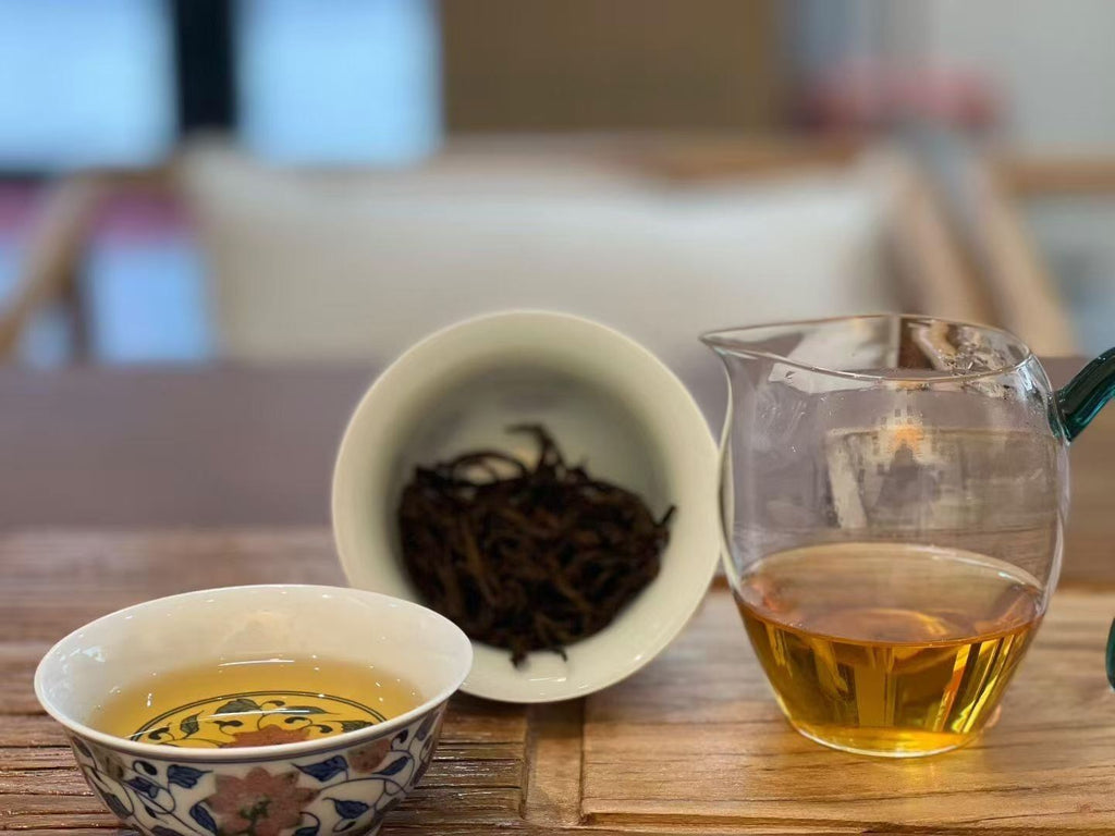 Tea-making setup with dry tea leaves, brewed tea in a cup, and a glass container on a wooden surface. Yunnan nuoxiang black tea with a natural glutinous rice aroma. Mellow, warming, deeply comforting. A daily ritual tea for stress relief and quiet evenings.