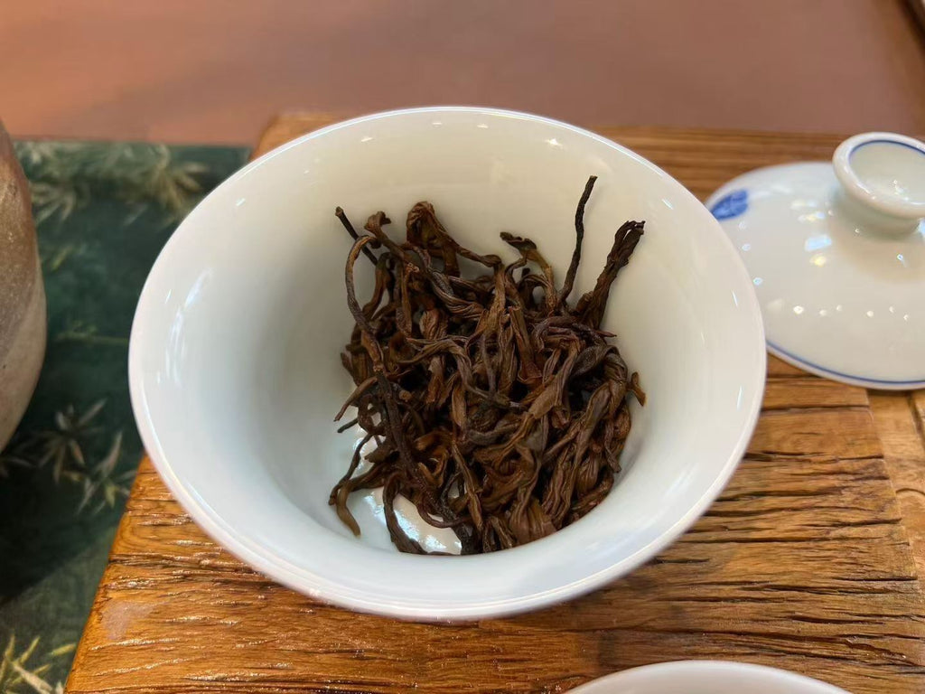 White bowl with dried tea leaves on a wooden table. Yunnan nuoxiang black tea with a natural glutinous rice aroma. Mellow, warming, deeply comforting. A daily ritual tea for stress relief and quiet evenings.