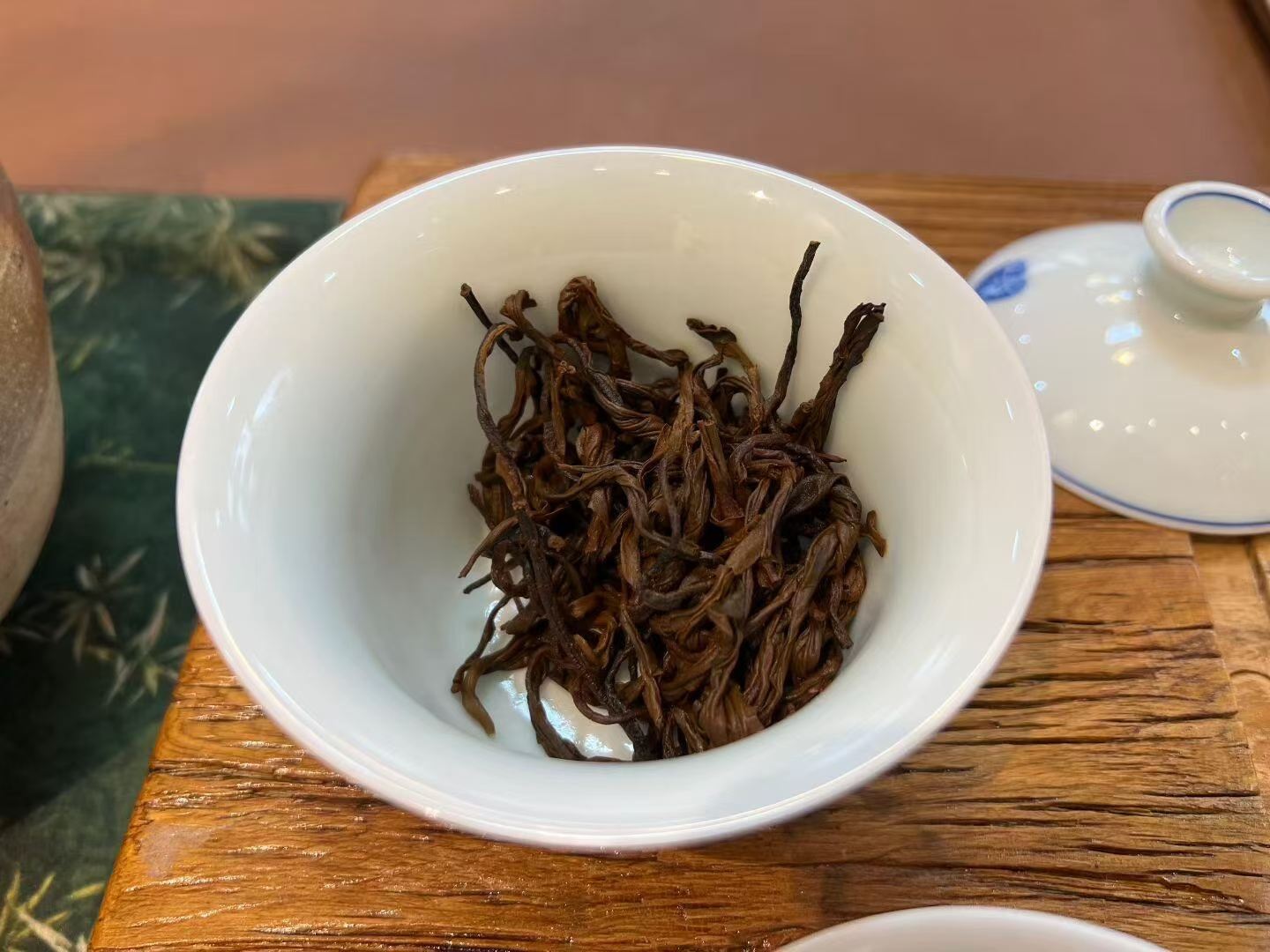 White bowl with dried tea leaves on a wooden table. Yunnan nuoxiang black tea with a natural glutinous rice aroma. Mellow, warming, deeply comforting. A daily ritual tea for stress relief and quiet evenings.