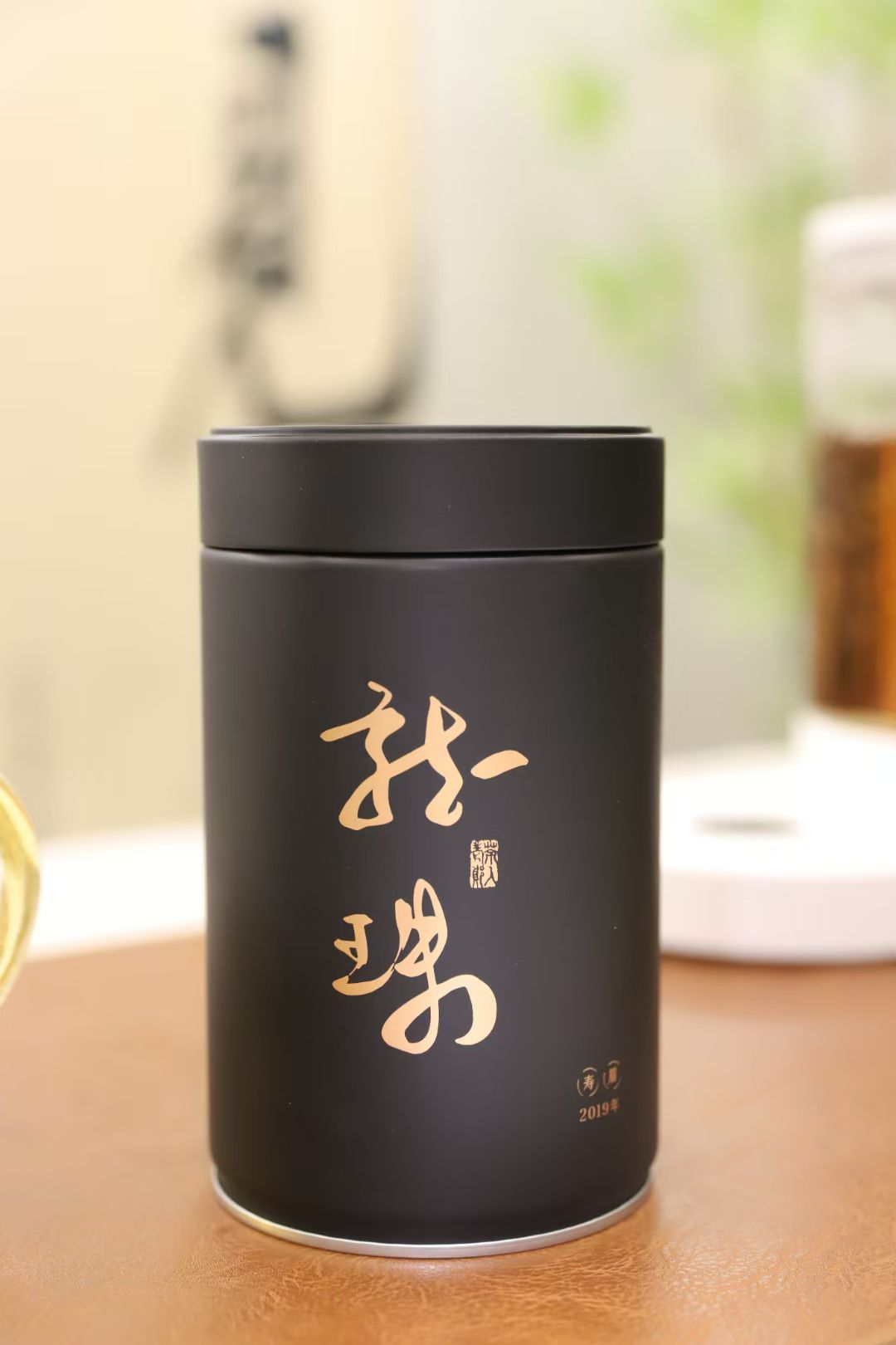 Black tea canister with gold text on a wooden surface inside is white tea