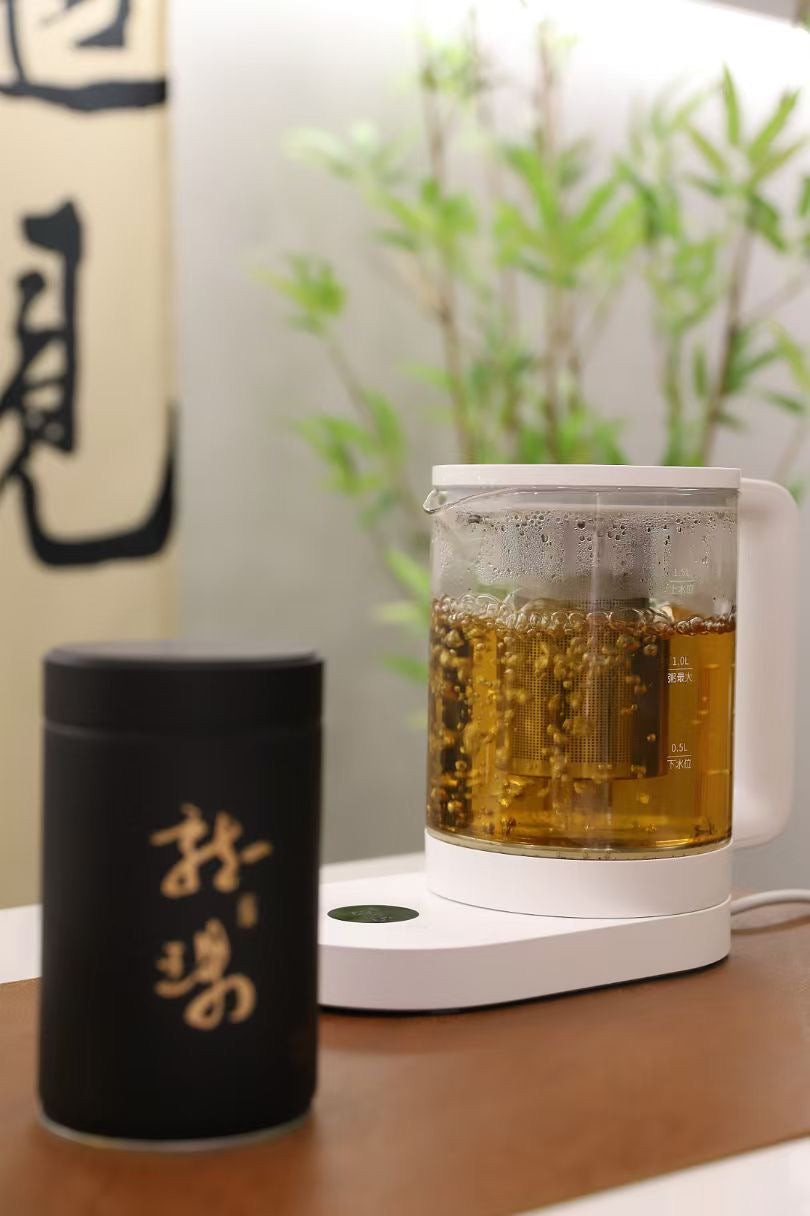 Tea-making setup with a glass teapot and black container on a wooden surface.